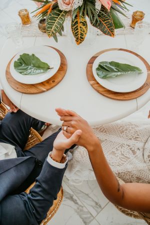 Wedding table setting with wooden chargers and tropical leaves on white tablecloth.