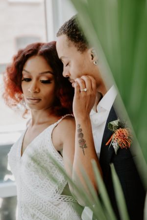 Romantic wedding portrait through green foliage with soft lighting.