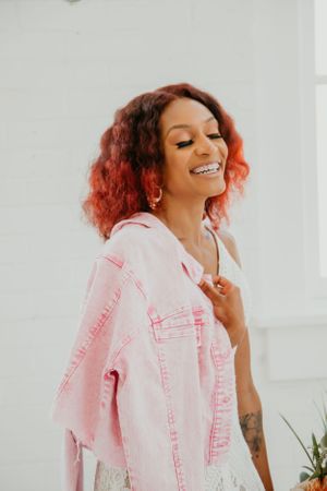 Person wearing pink denim jacket poses playfully against white wall.