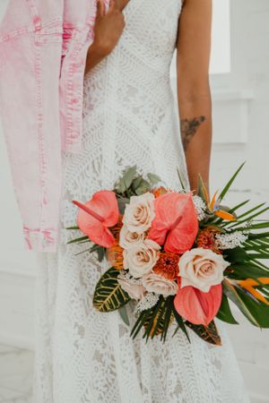 Tropical wedding bouquet with coral flowers and palm leaves against a lace dress.