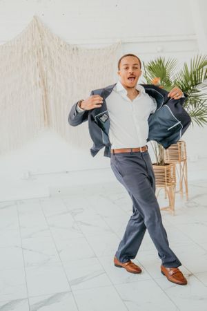 Person in navy suit dances energetically in bright white room.