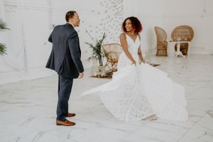 A couple in wedding attire playfully interacts in a bright white studio setting.