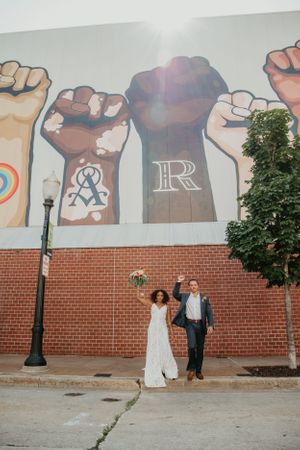 Wedding couple poses playfully in front of a street art mural with raised fist designs.