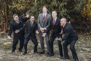 Groomsmen in dark suits pose playfully outdoors during wedding photoshoot.