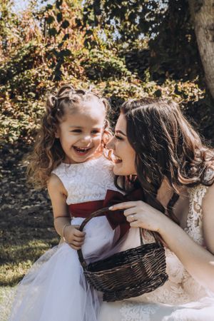 A joyful moment shared between two people in white dresses with a woven basket in an outdoor garden setting.