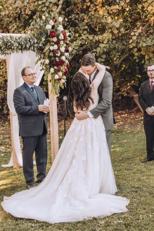 A romantic outdoor wedding ceremony under an arch decorated with red and white flowers.
