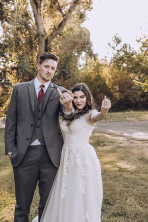 A couple in wedding attire poses playfully while showing their rings to the camera.