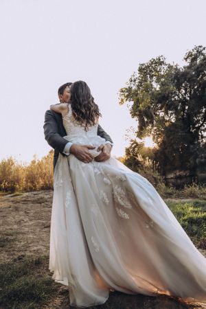 A romantic sunset wedding portrait with a flowing white dress in a natural outdoor setting.
