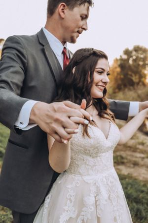 A couple shares a joyful dance moment in their wedding attire outdoors.