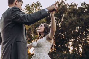 A couple dances together in wedding attire against a sunset backdrop.