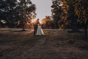 Wedding couple silhouetted against a glowing sunset through autumn trees.