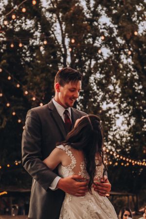 Romantic first dance under string lights at outdoor wedding reception.
