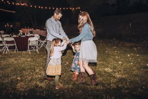 Wedding guests dancing and celebrating on lawn under string lights at dusk.