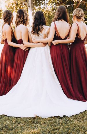 Back view of bridesmaids in burgundy dresses standing with bride in white gown.