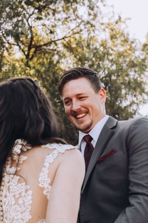 Couple sharing intimate wedding moments outdoors with sunlit trees in background.