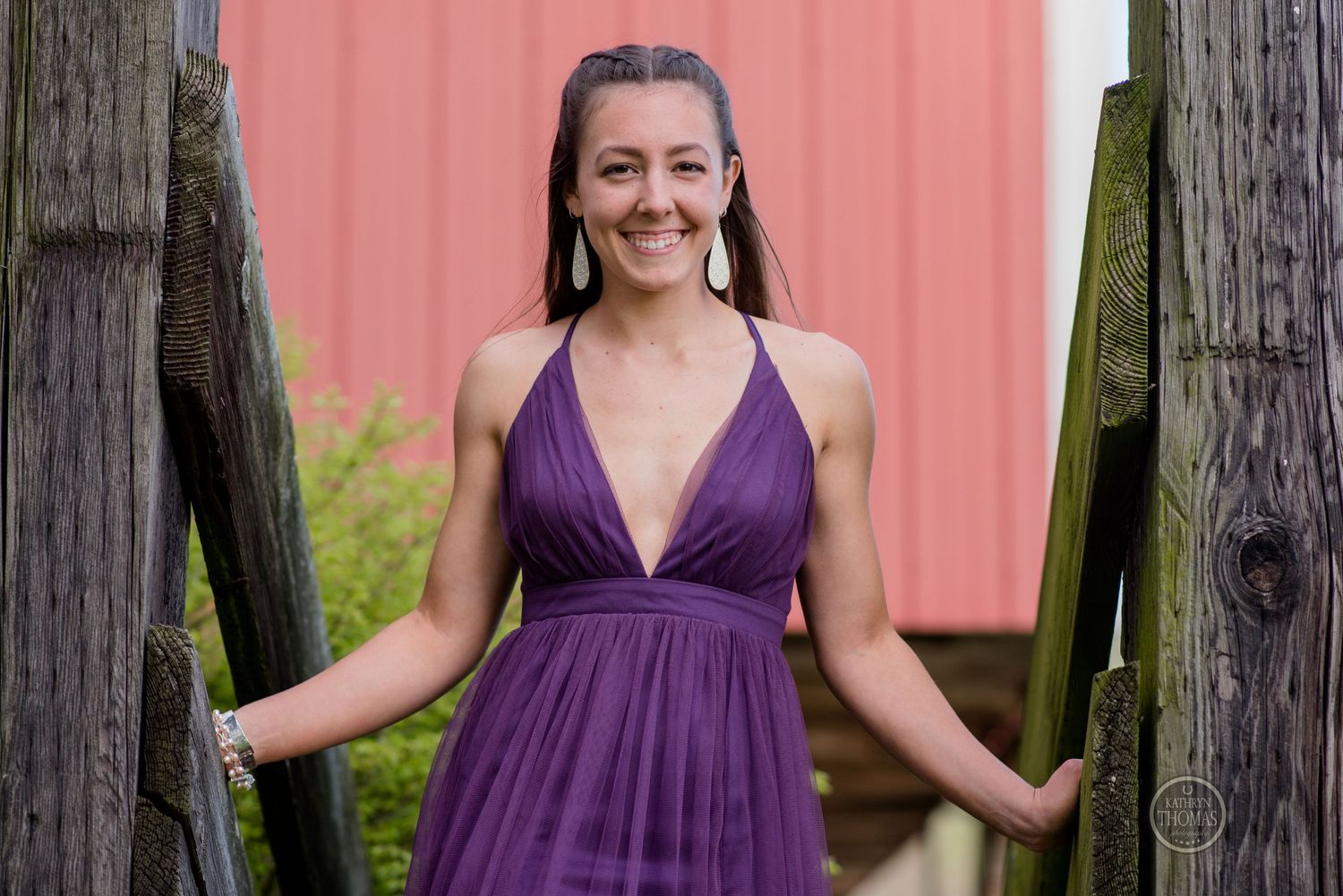 A joyful pose between wooden posts with a pink barn wall in the background.