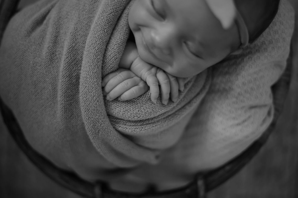 Black and white portrait of sleeping newborn swaddled in soft blanket.