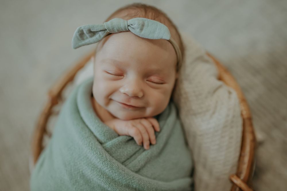 Smiling newborn baby wrapped in mint green swaddle with matching bow headband.