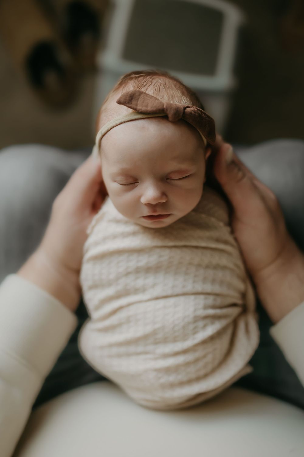 Overhead view of sleeping newborn wrapped in cream fabric with brown headband.