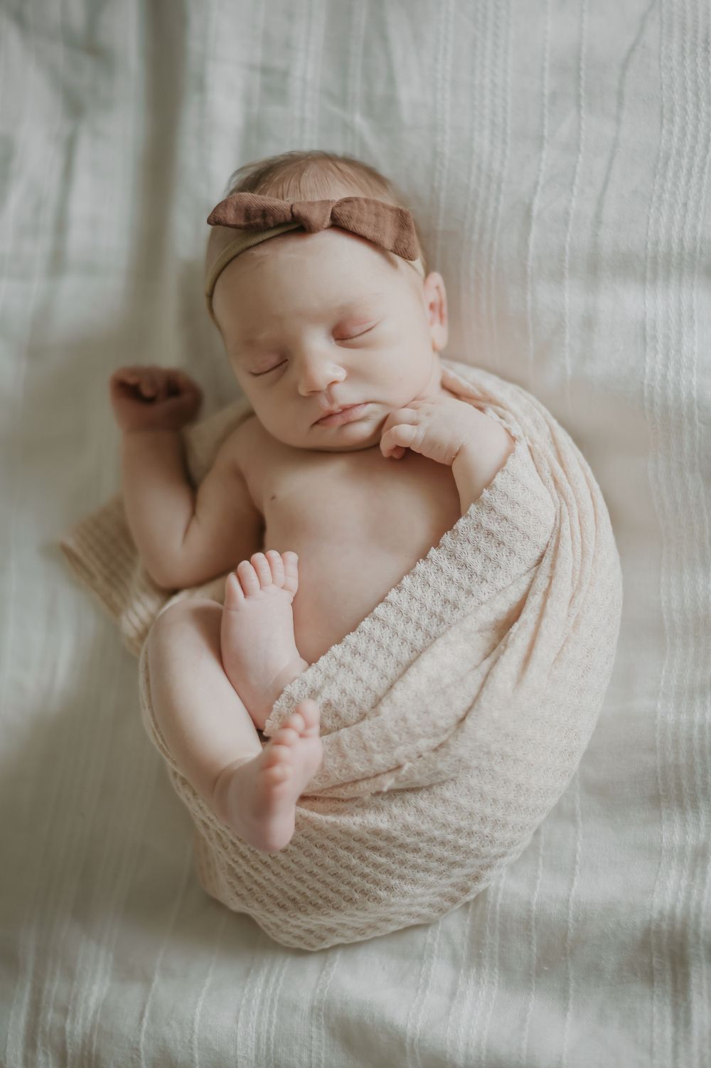 Peaceful newborn baby swaddled in textured cream blanket resting on white bedding.