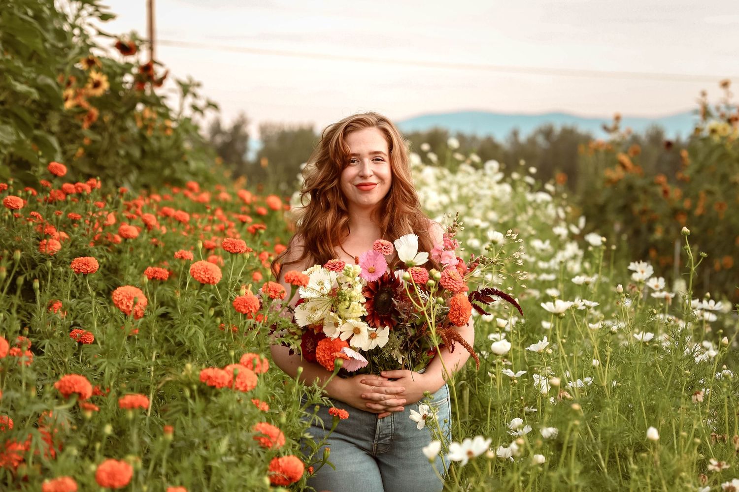 Portrait of person holding colorful bouquet in field of orange poppies and white daisies.