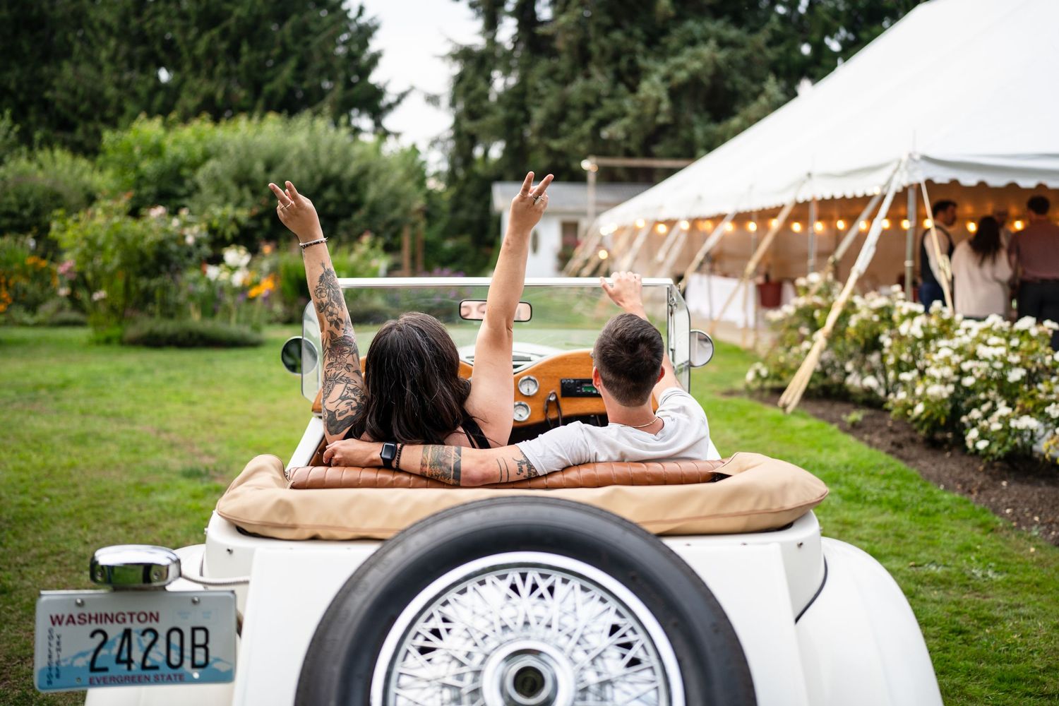 Couple poses playfully in vintage car during wedding celebration.