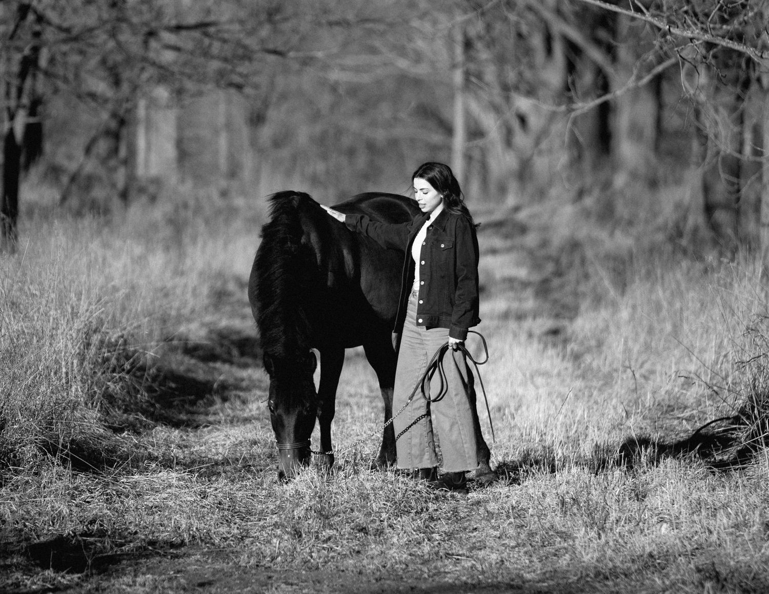 Black and white photograph of a person walking alongside a dark horse in a winter field.
