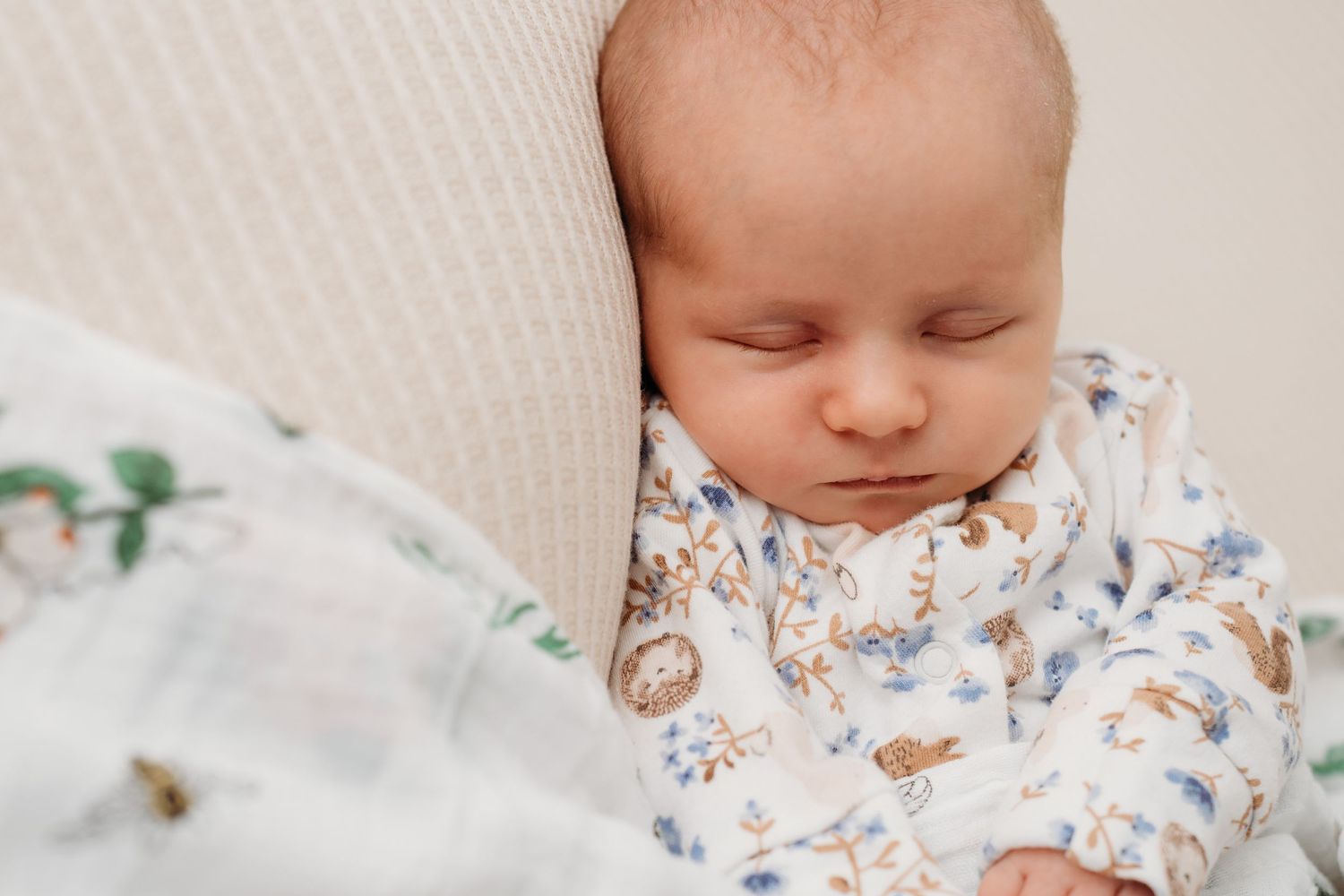 Sleeping baby wearing floral print outfit resting on white textured surface.