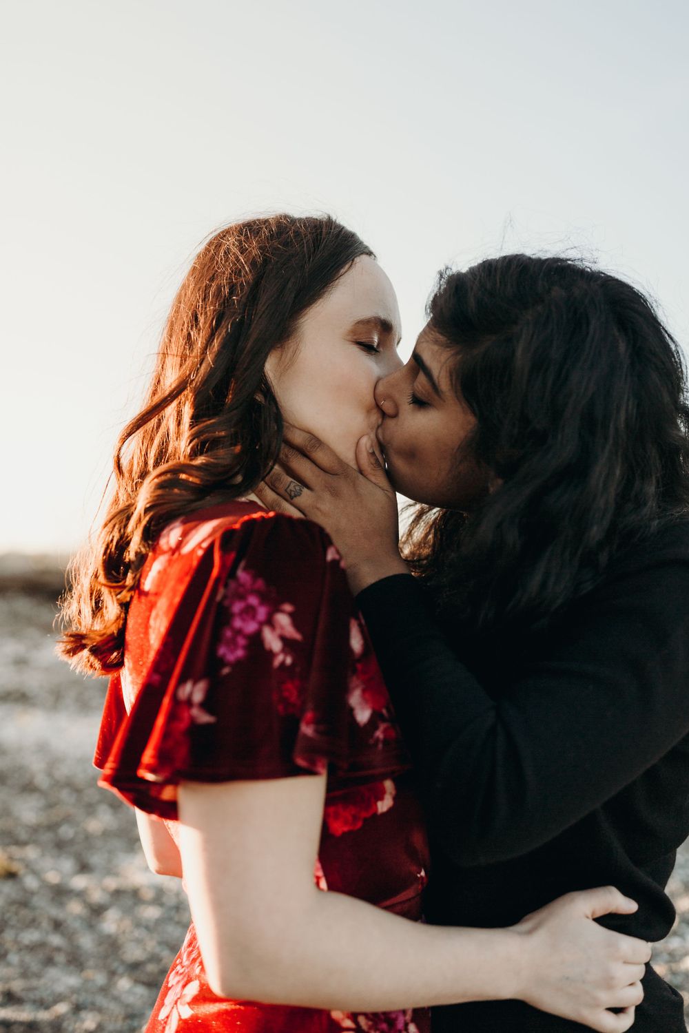 Intimate romantic moment between couple at sunset in red floral dress and black outfit.