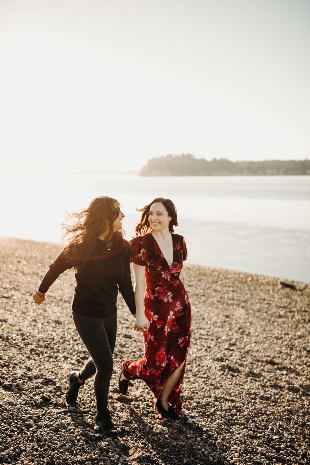 Two people running and laughing together on beach at golden hour.