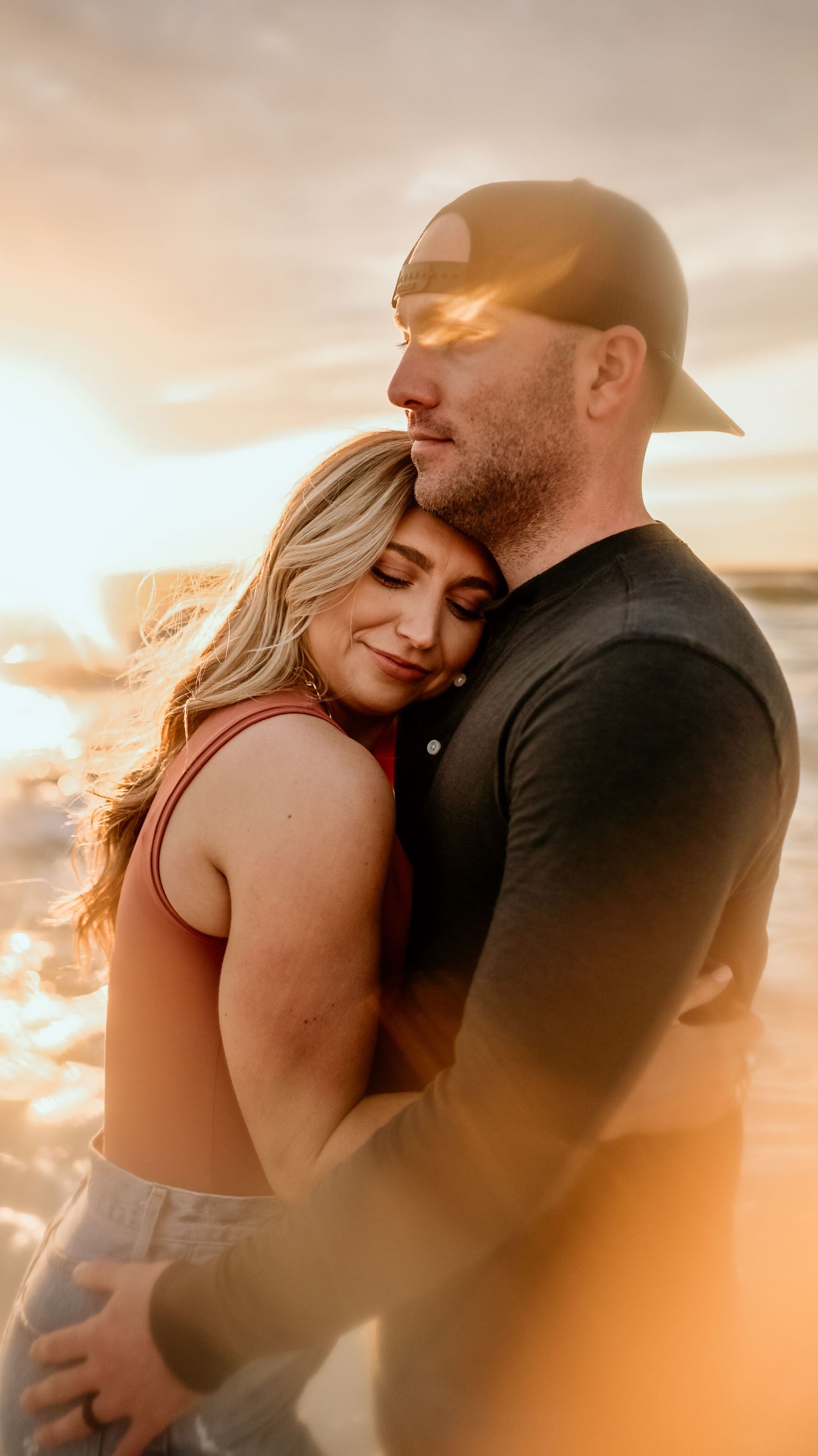 Intimate sunset embrace on beach with golden light filtering through.