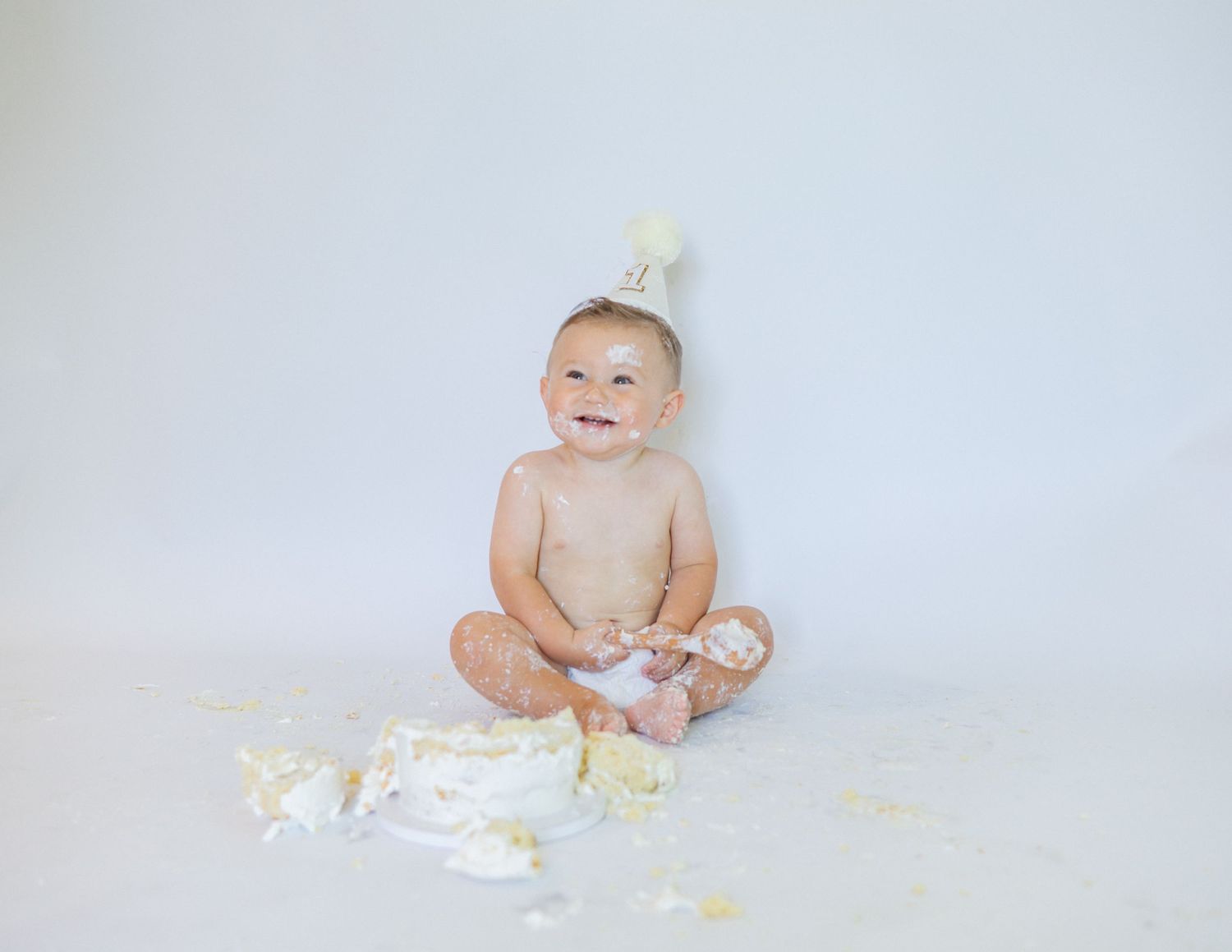 Baby wearing a crown sits on white background surrounded by scattered confetti.
