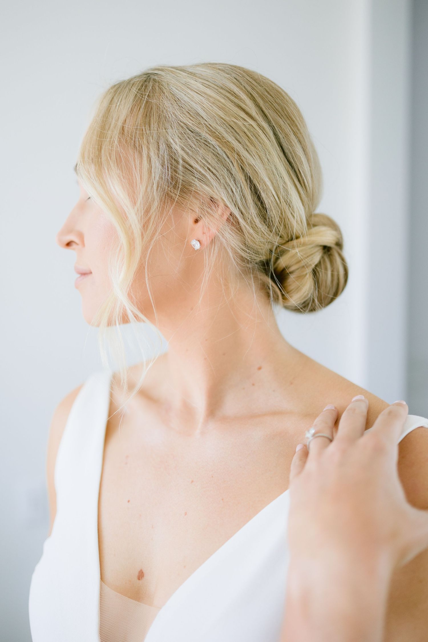 Elegant bridal hairstyle with low bun and delicate white dress detail shown in profile.