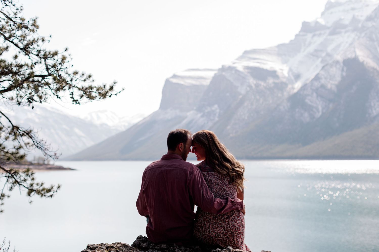 Couple sits overlooking pristine mountain lake surrounded by snow-capped peaks.