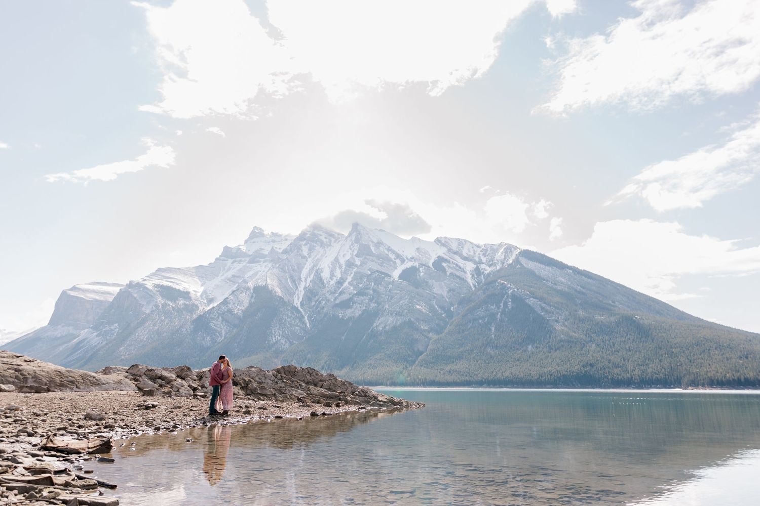 Rocky mountain shoreline frames beautiful lake and snow-capped peak landscape.