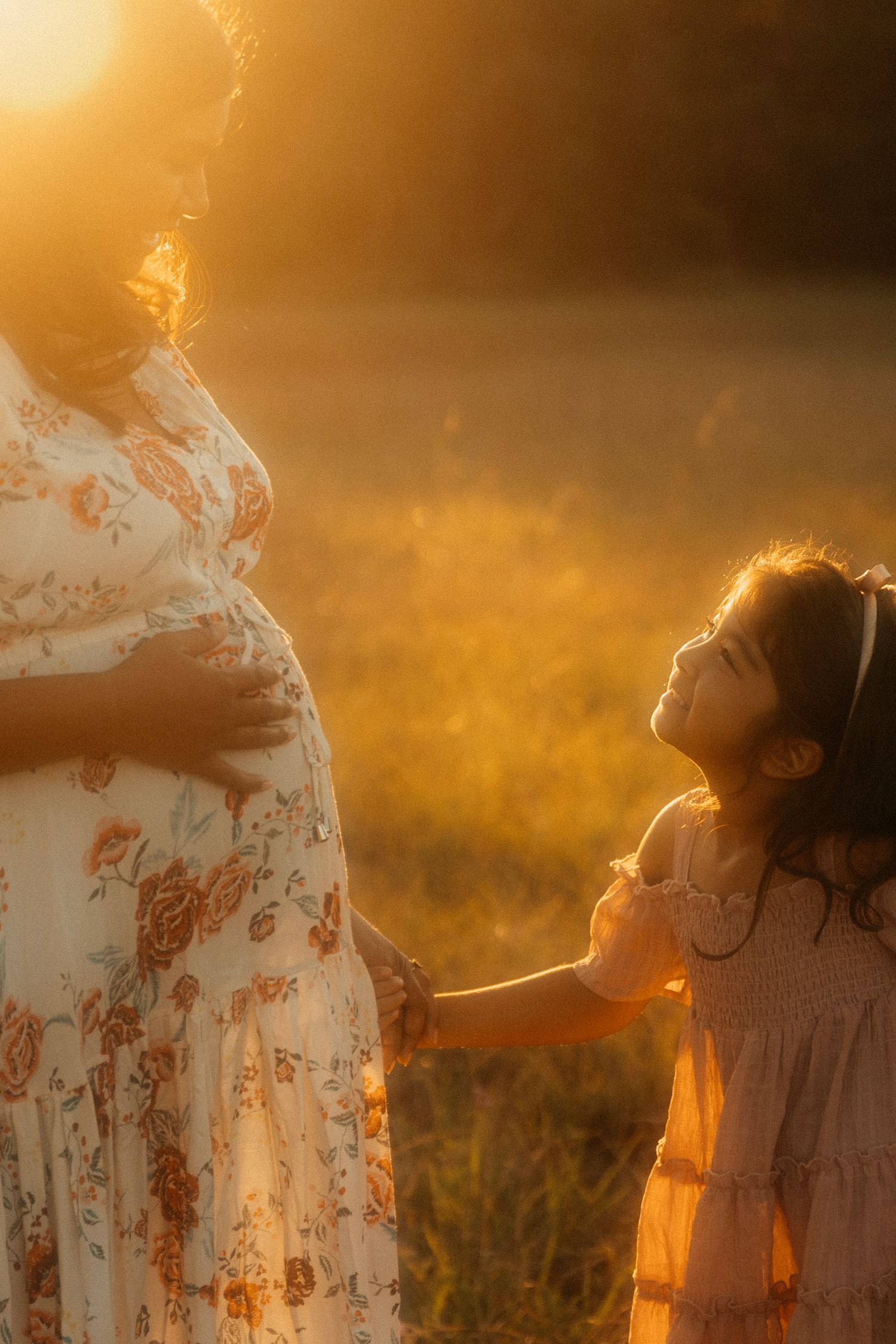 Children playing together in a golden field at sunset while adult watches.