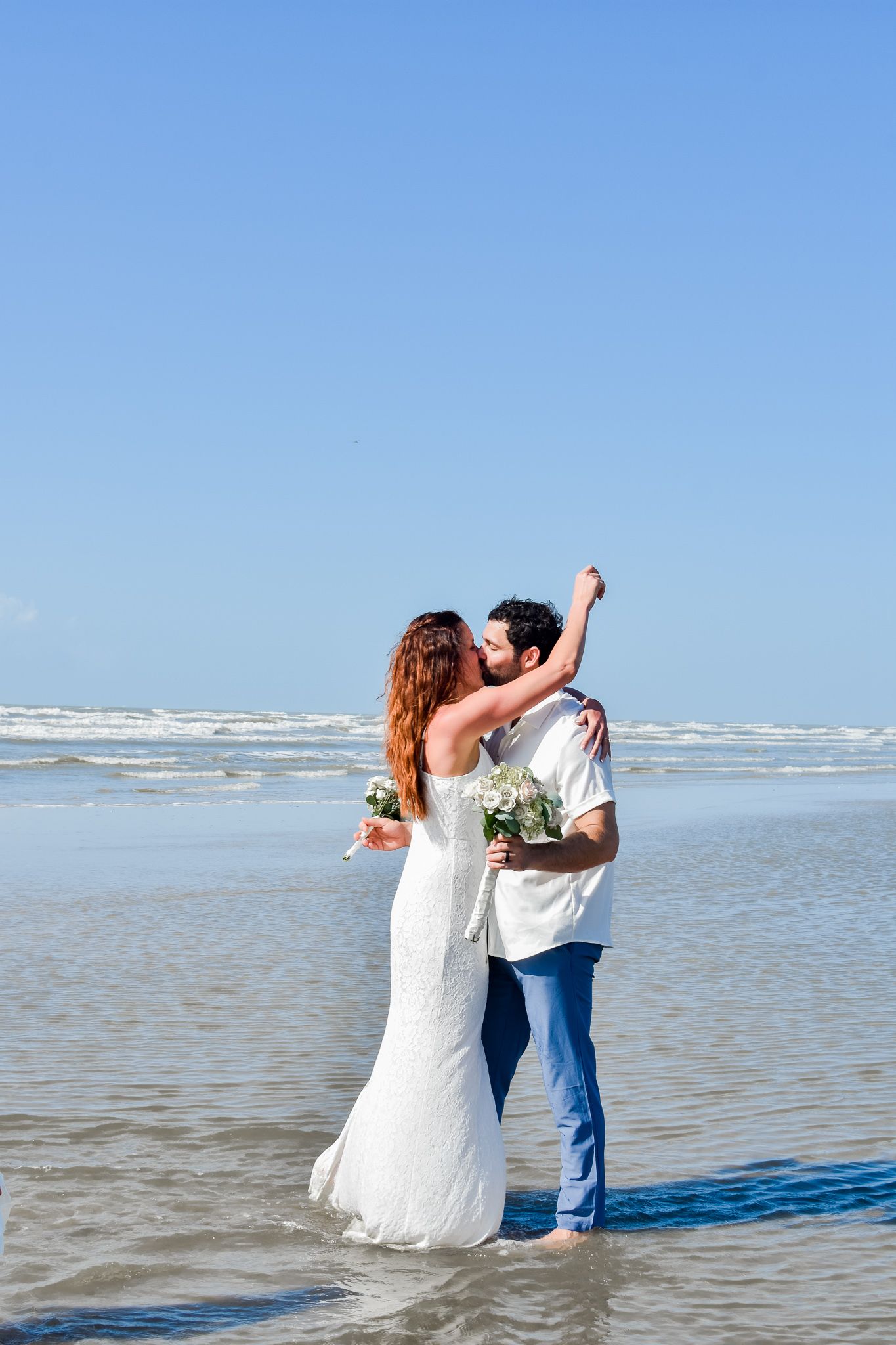 A romantic beach wedding portrait with waves and blue sky in the background.