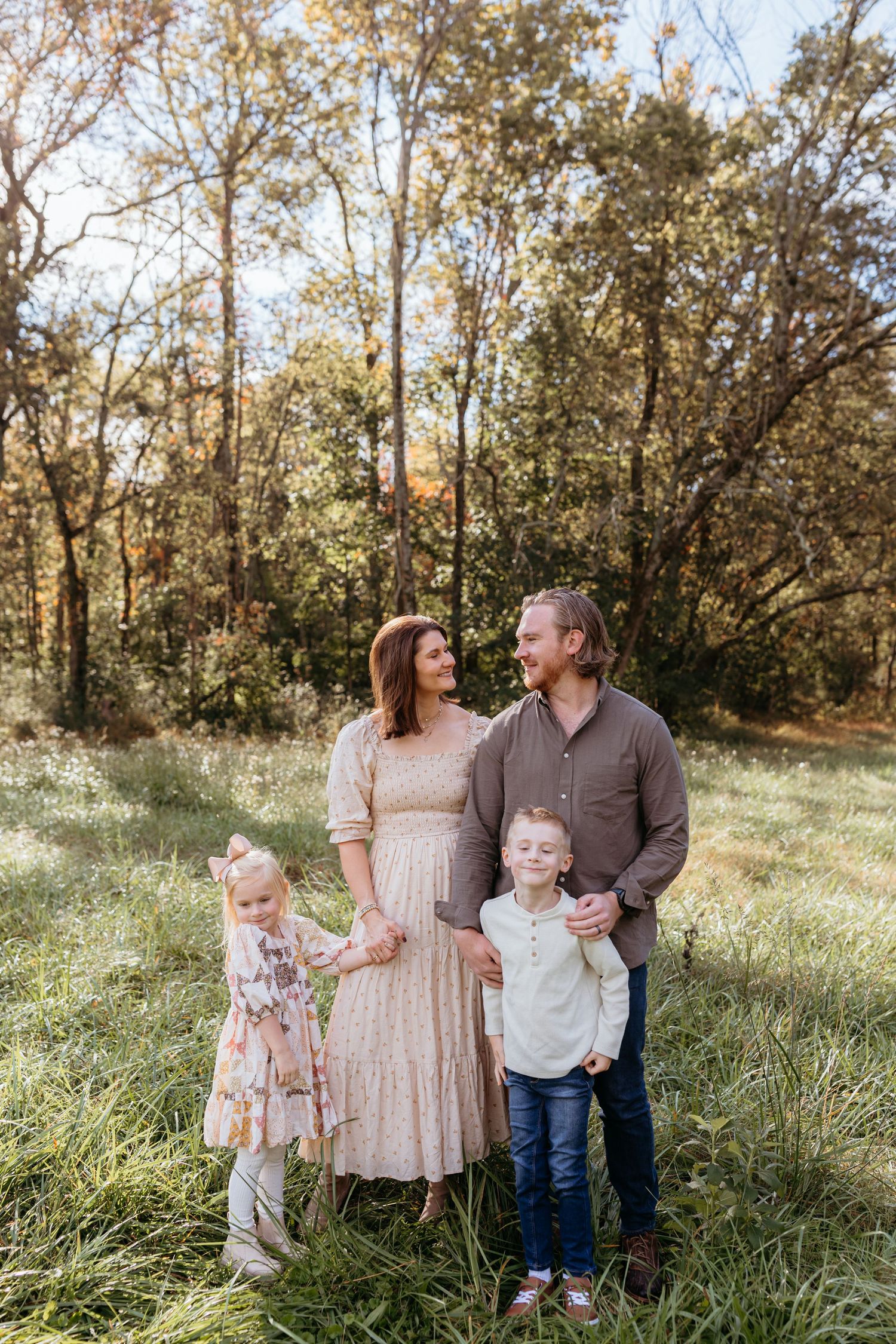 Family of four smiling together in outdoor fall setting.