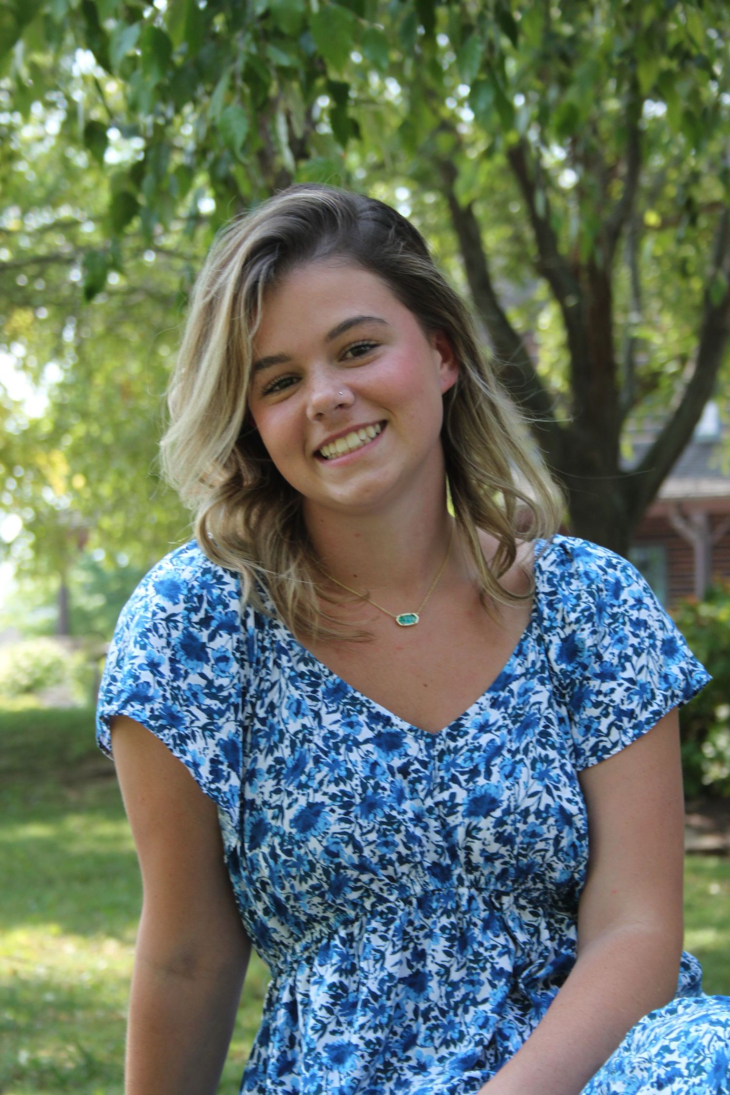 Girl smiling in front of trees at College of the Ozarks for senior pictures.