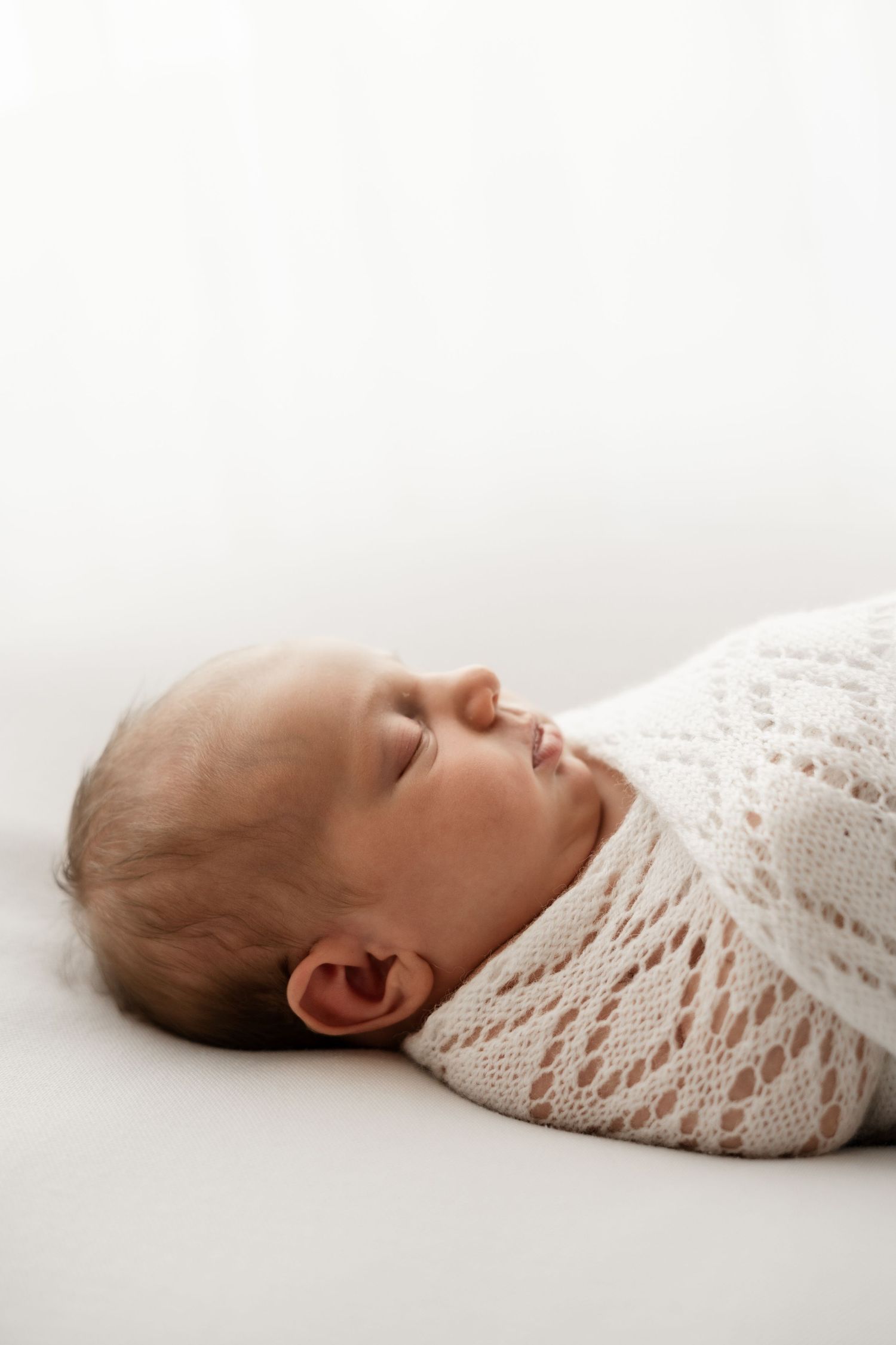 Swaddled newborn baby sleeping on white background wrapped in lace knit blanket.