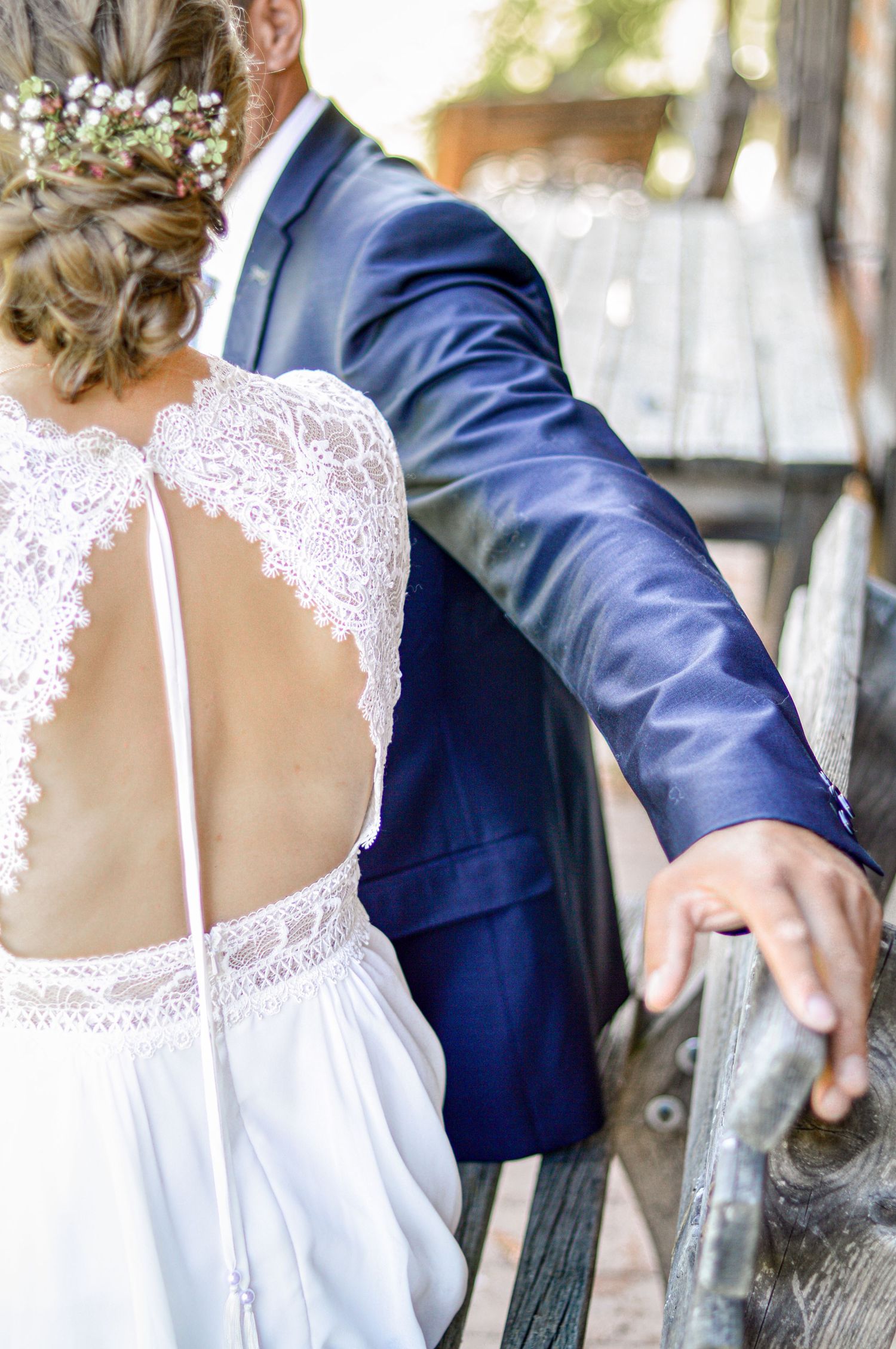 Eine Braut in einem weißen Hochzeitskleid mit Spitzenrücken sitzt neben dem Bräutigam, der eine marineblaue Anzugsjacke trägt.
