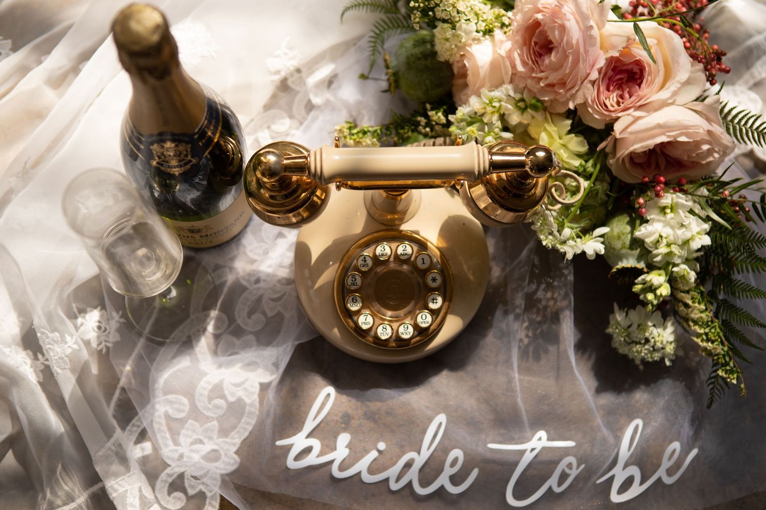 Wedding preparations with champagne and flowers on floor beside white dress detail.