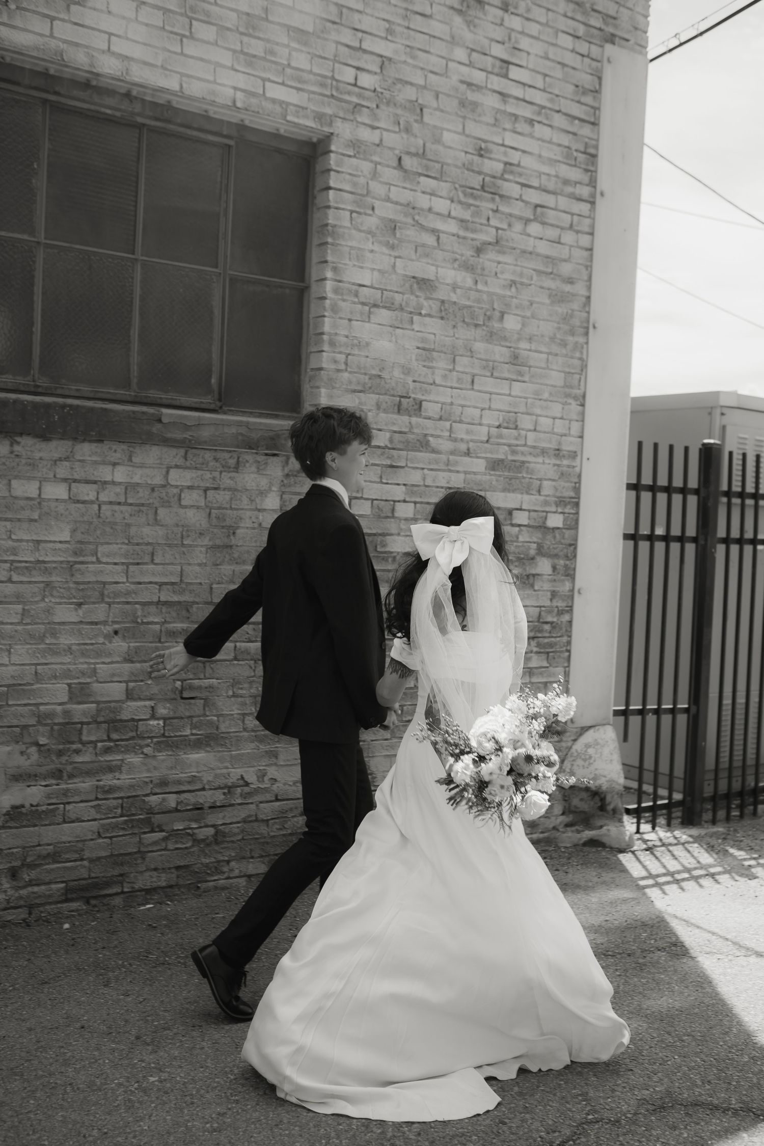 Candid moment of a couple in wedding attire sharing laughter by brick wall.