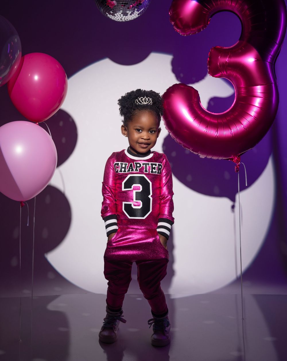 Purple and pink party setup with disco ball and large pink number 3 balloon against spotlit background.