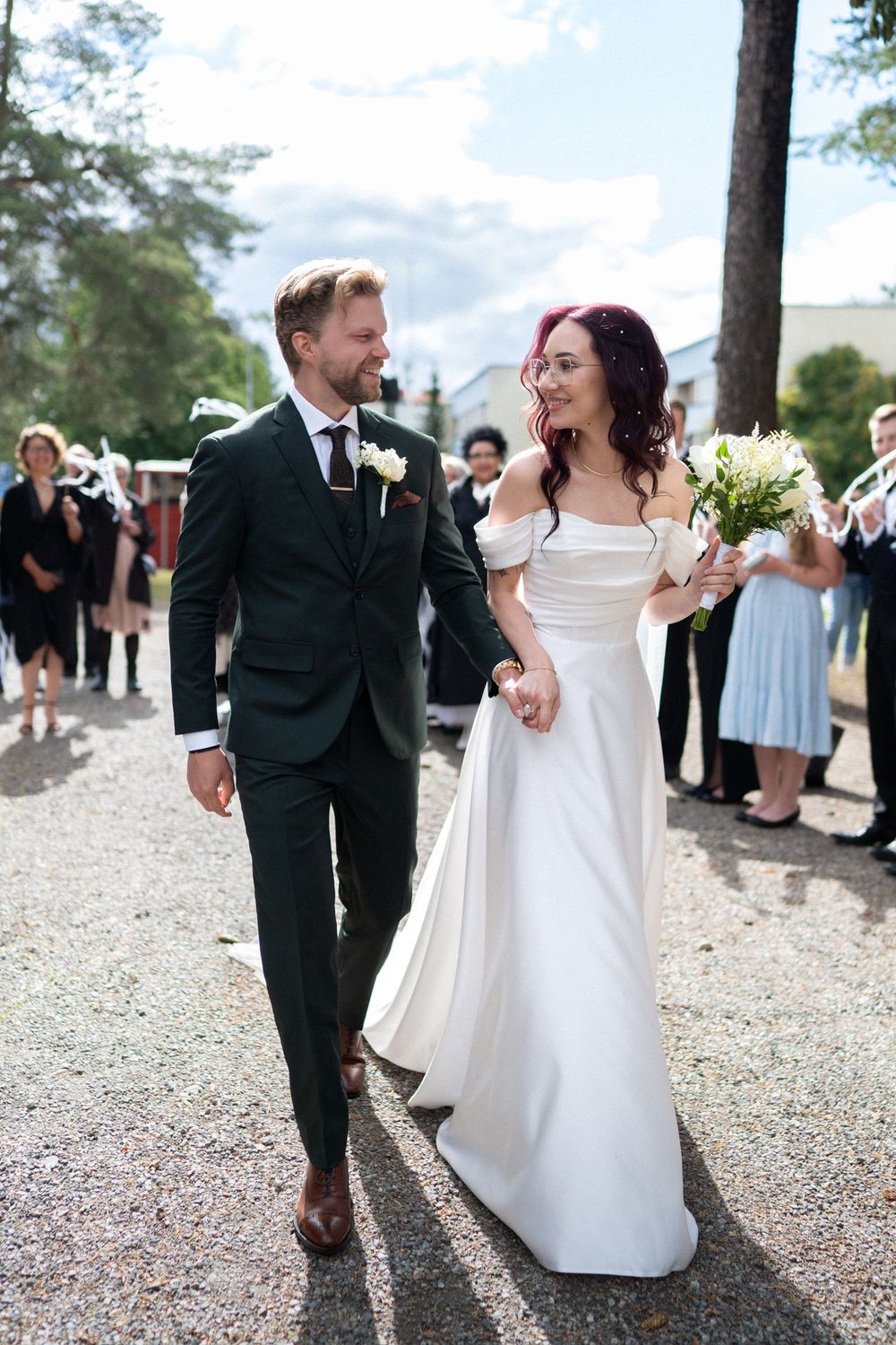 Wedding couple shares joyful dance together on a gravel path surrounded by trees and guests.
