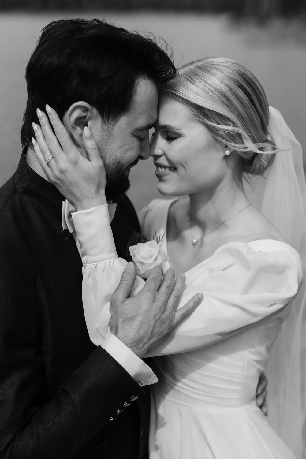 A romantic black and white wedding photo showing an intimate moment between a bride in white and groom in dark attire.