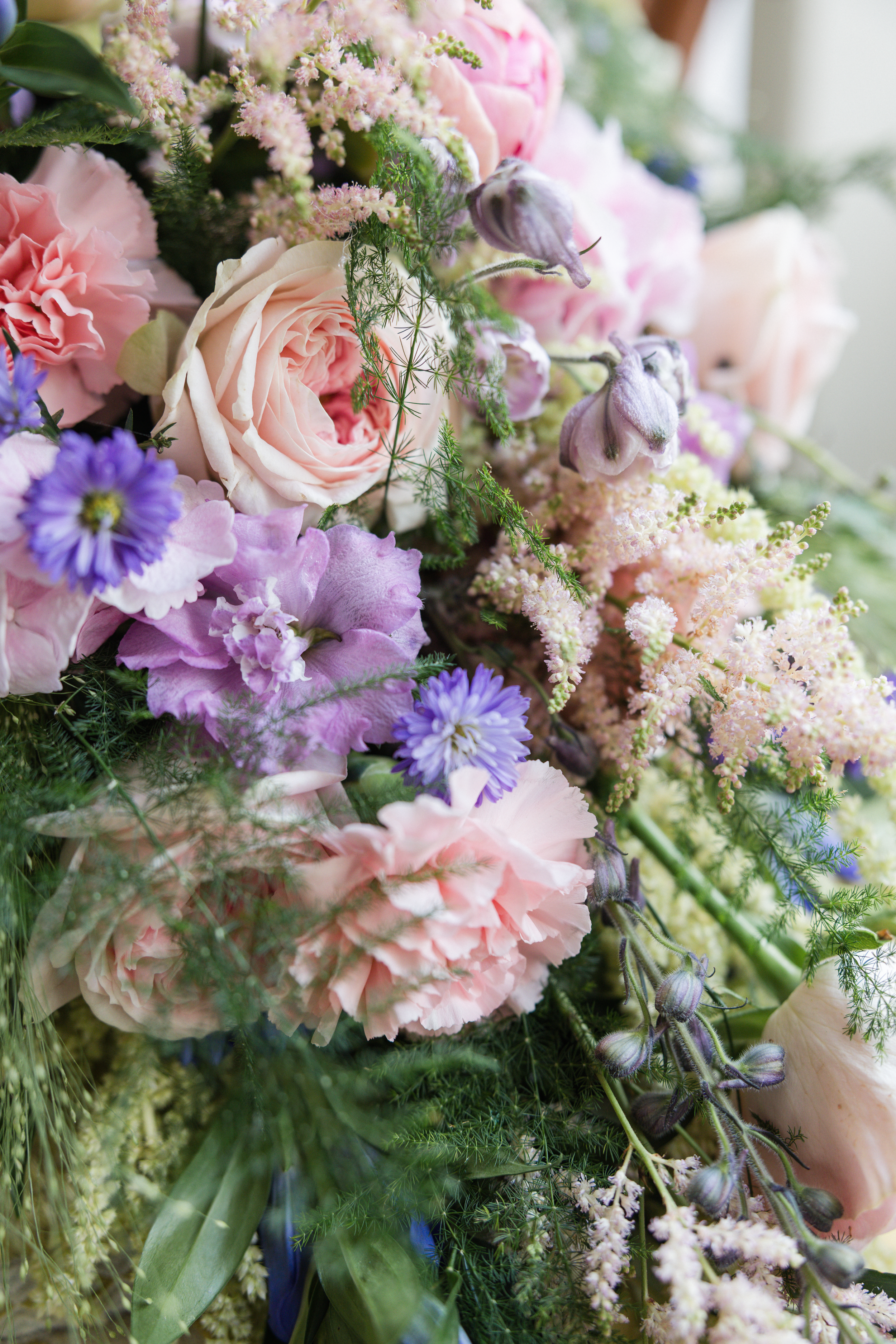 Beautiful floral arrangement featuring pink roses, purple daisies and delicate greenery in soft pastel colors.