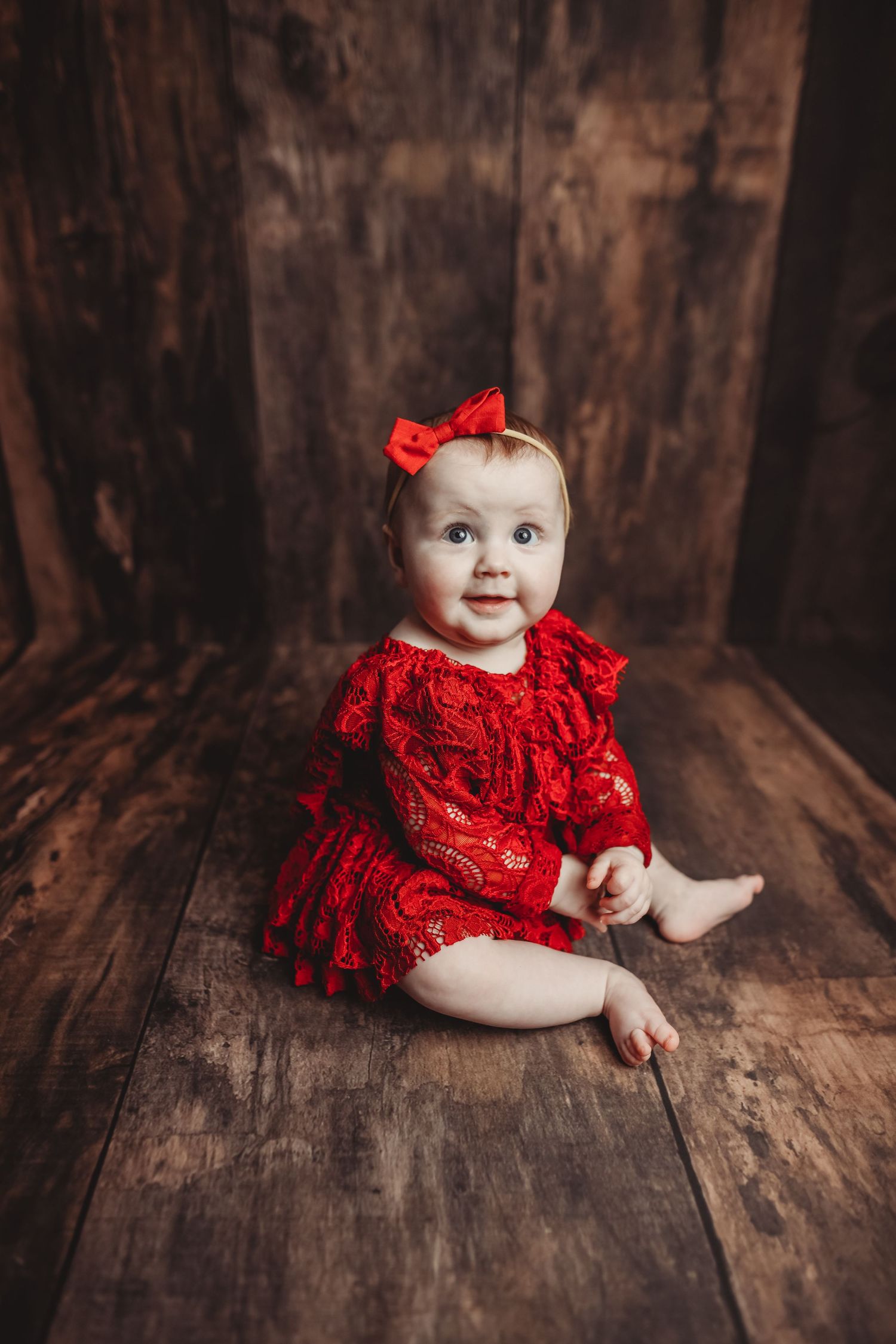 Bright red lace dress against dark wooden backdrop in studio setting.
