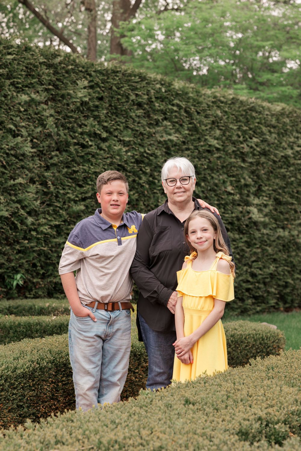 A group poses by tall manicured hedges in a formal garden setting wearing casual attire.