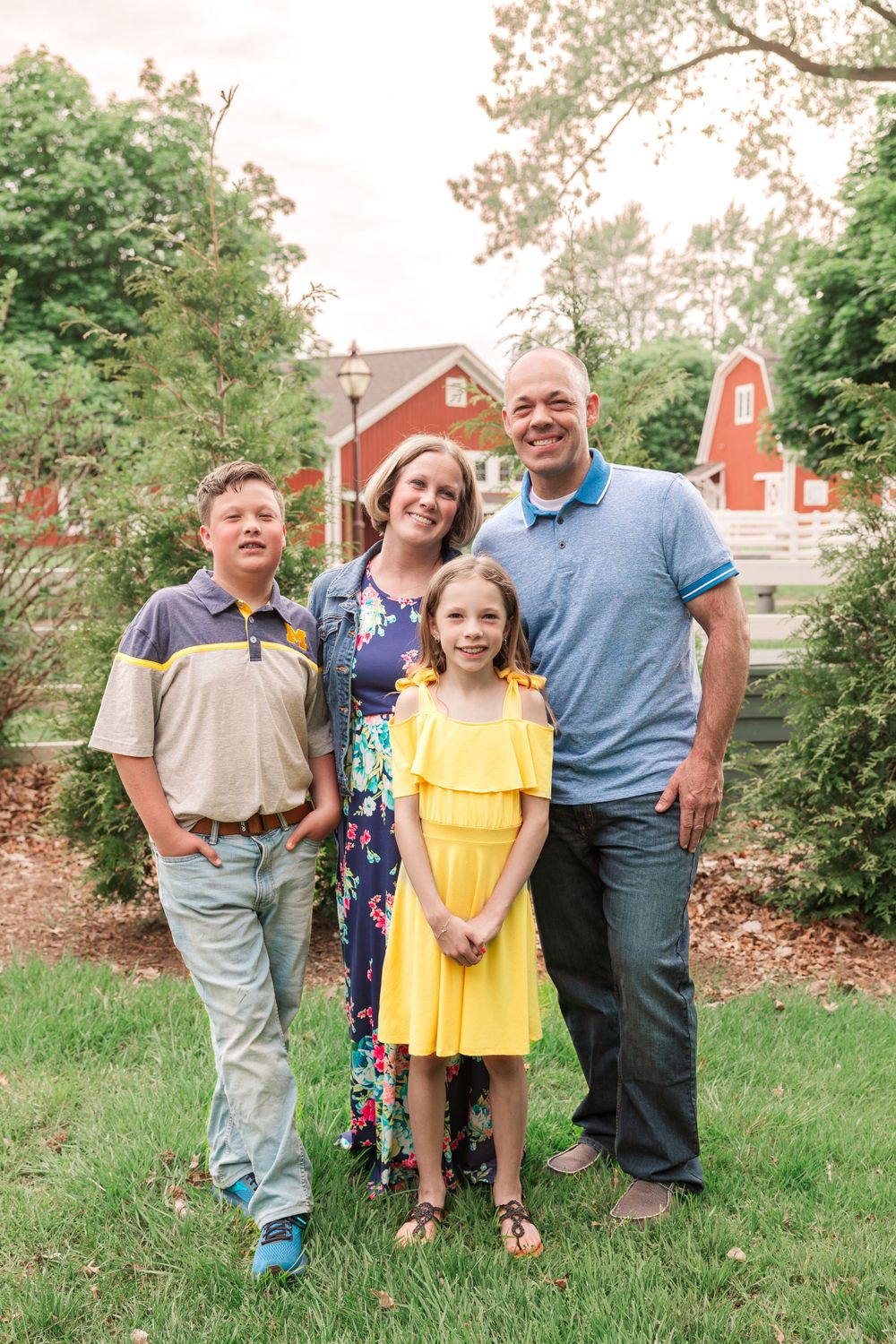Family of four posed together with red barn visible in background.